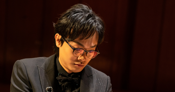 Classical pianist Anson Tang in formal black attire playing a concert grand piano on stage.