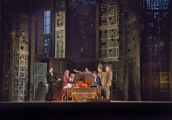 A group of 7 stand around a bed on stage. 