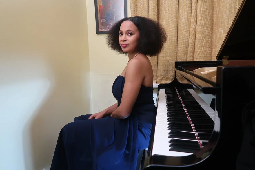 Pianist Rebeca Omordia in a dark blue gown, seated at a black grand piano.