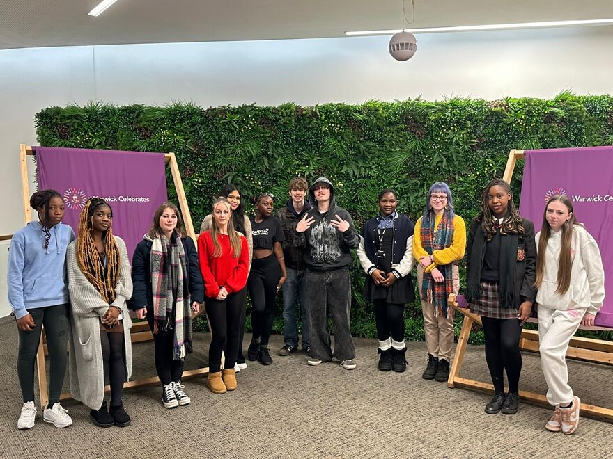 Group of young people in front of two large purple chairs and a hedge