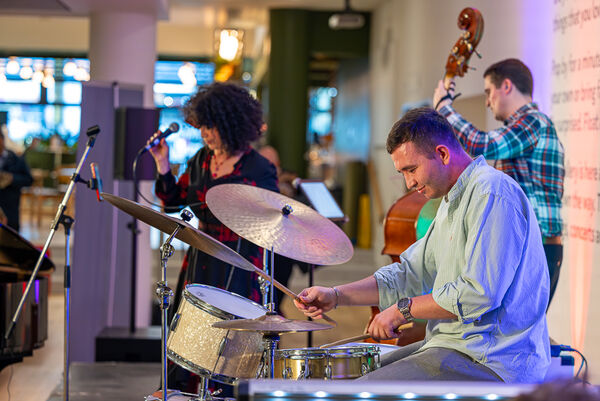 Singer holding microphone, person playing drums and person playing double bass