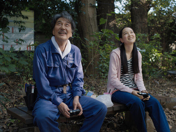 An older man and young teenage girl sit together smiling in a park. 
