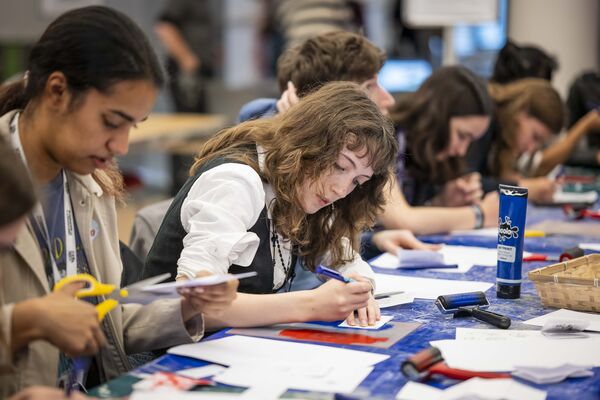 Students cutting paper and preparing stencils around an ink-splattered workshop table.