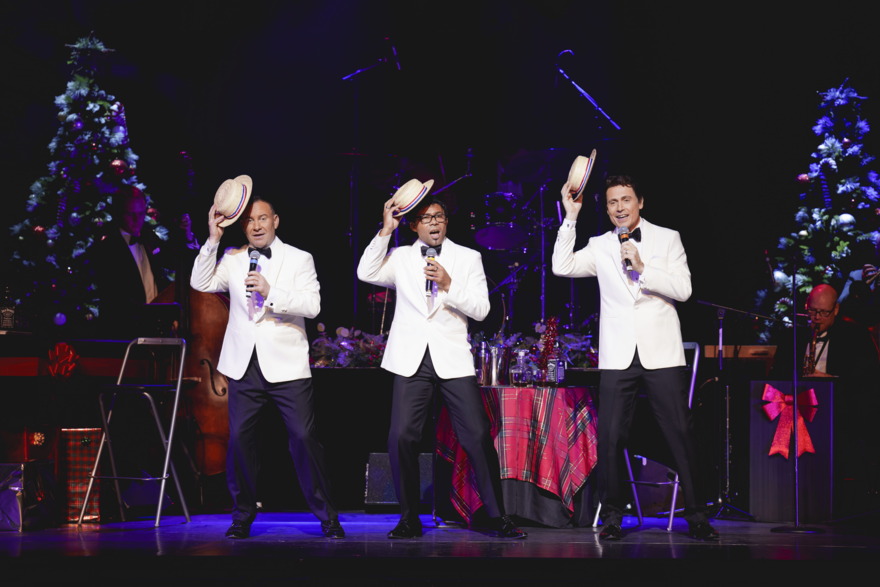 3 Singers in white tuxedoes holding microphones and hats 