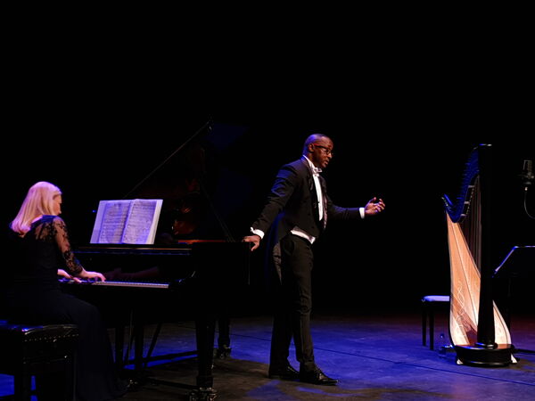 Man stood in a tuxedo with a woman sat playing the piano