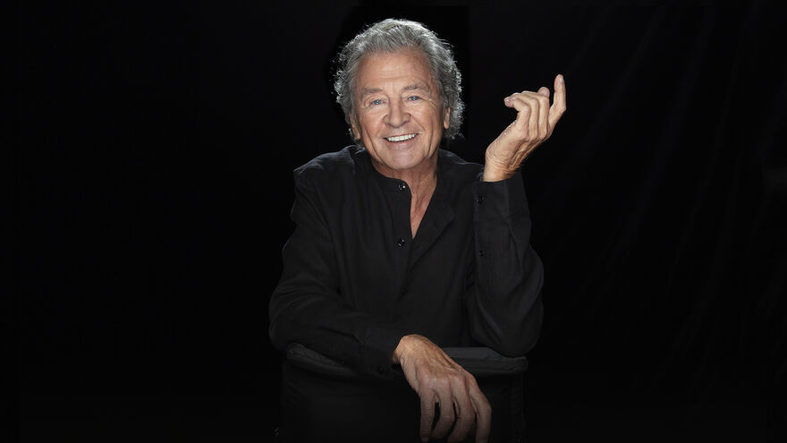 Ian Gillan smiles at the camera with his hand in the air 