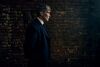 Cillian Murphy as Tommy Shelby. He is standing in front of a brick wall wearing a suit. 