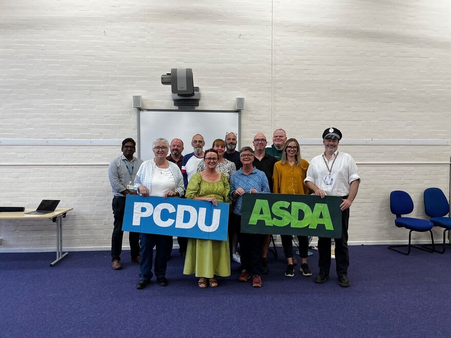 Group of people holding up signs, signs read 'PCDU' and 'ASDA'