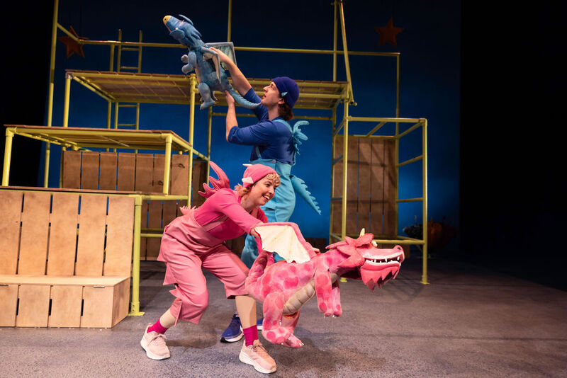 Two actors in pink and blue costumes playfully operate large, colourful dragon puppets on the stage of the Zog theatre production.
