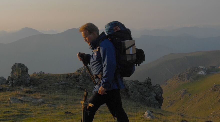 An older man walks the Camino de Santiago. He carries a large rucksack.