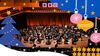 An orchestra on stage surrounding by Christmas illustrations