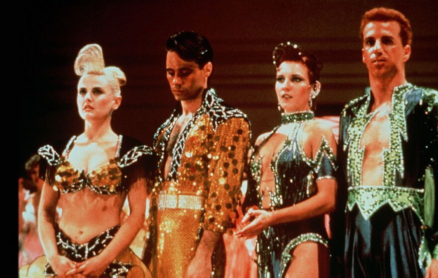 Two couples line up on a dancefloor, all wearing bright and sparkly outfits. 
