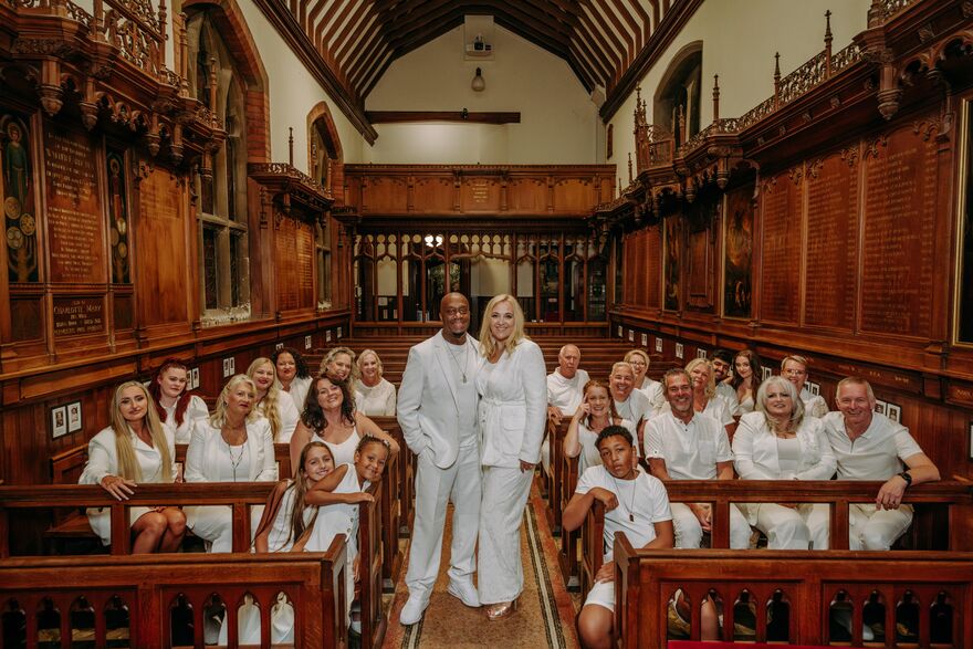 A choir sat down in chruchs pughs with two members stood in the aisle 