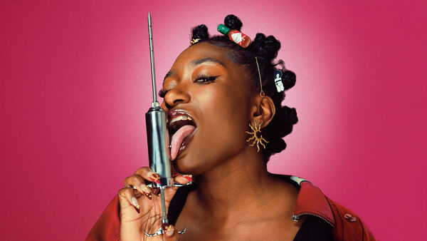 Sophie licks a big syringe in front of a pink background
