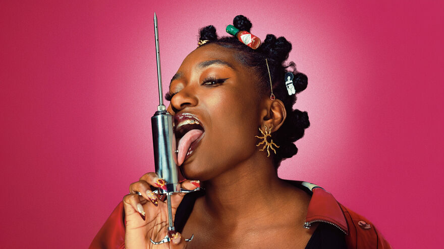 Sophie licks a big syringe in front of a pink background