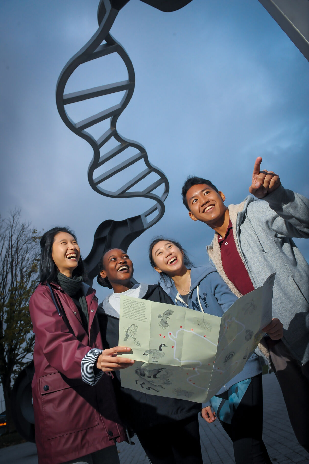 A group of students with a map underneath the Let's Not Be Stupid sculpture