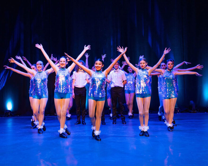 A group of dancers on stage with their arms in the air