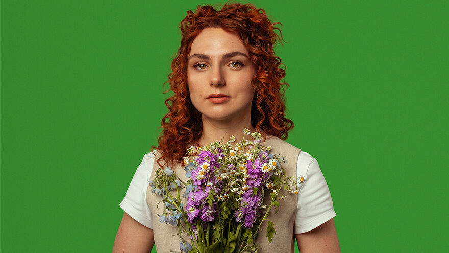 Ania Magliano holding a bunch of daisies and purple flowers in front of a green background
