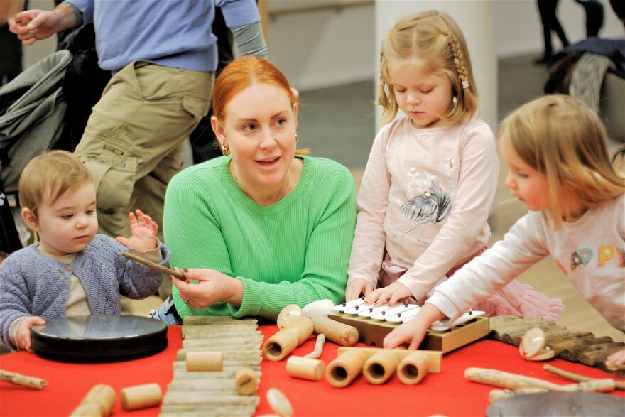A woman and three children playing with various musical instruments.