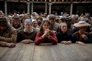 A woman stands at the front of a crowd at the Globe theatre. 