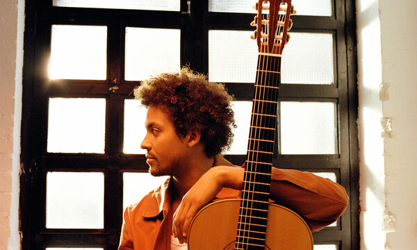 Plinio Fernandes sat in front of a window with his arm resting on a guitar