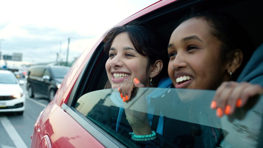 Two young women smile widely as they look out of a open car window. 
