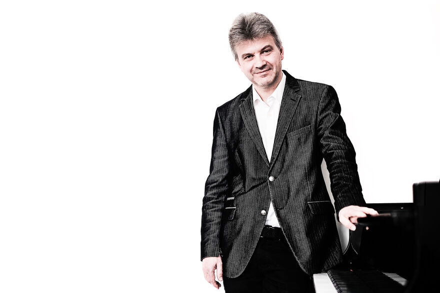 Mark Bebbington leaning against a piano against a white background
