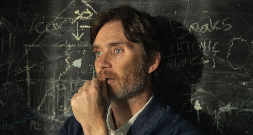 A male teacher rests against a blackboard covered in yellow chalk.