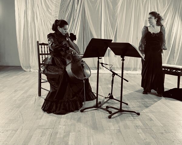A Cellist sat down and a singer stood up, both with music stands in front of them A Cellist sat down and a singer stood up, both with music stands in front of them