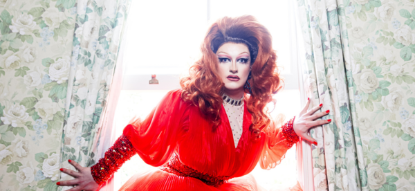Kate Butch in a red dress crouching in a window with floral curtains