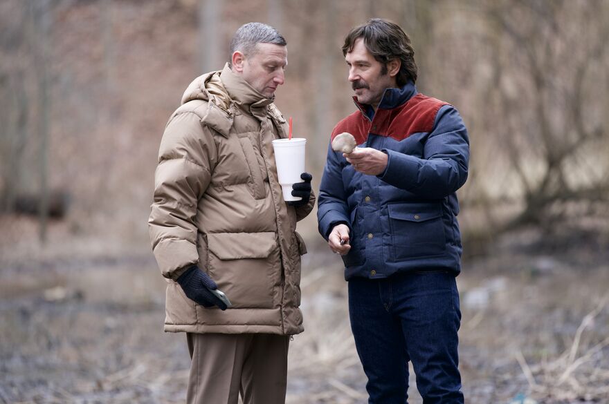 Two men stand together in a woodland.