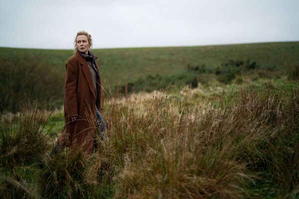 A woman stands on a grassy moor. 