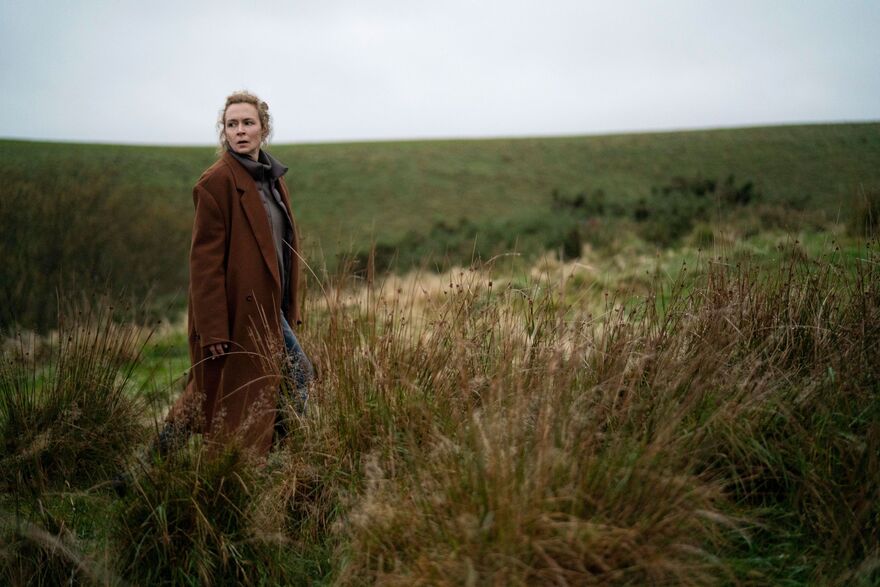A woman stands on a grassy moor.