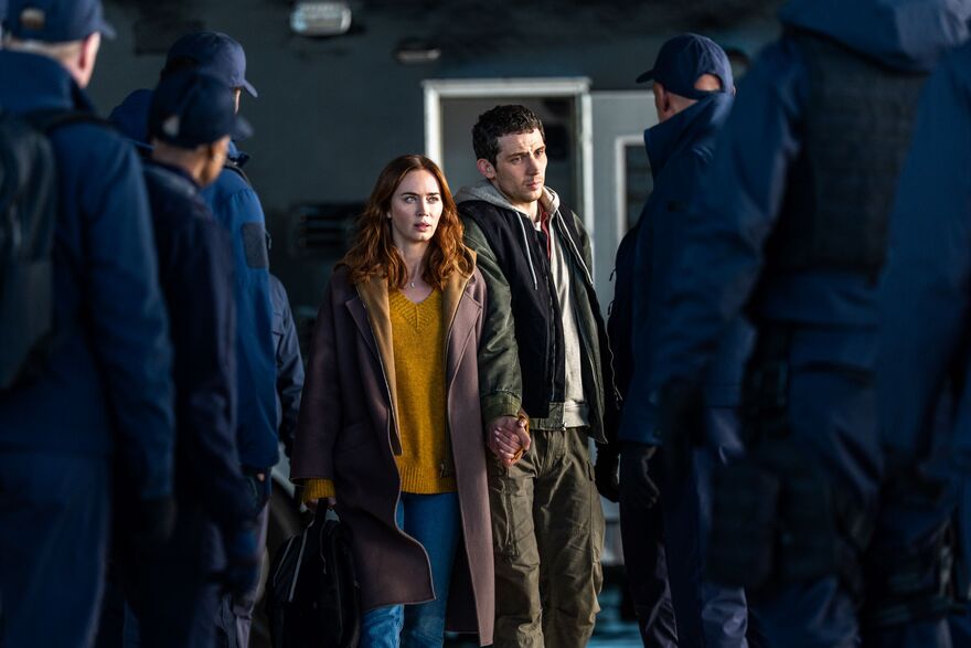 A man and woman hold hands walking through a group of people wearing matching blue jumpsuits.  