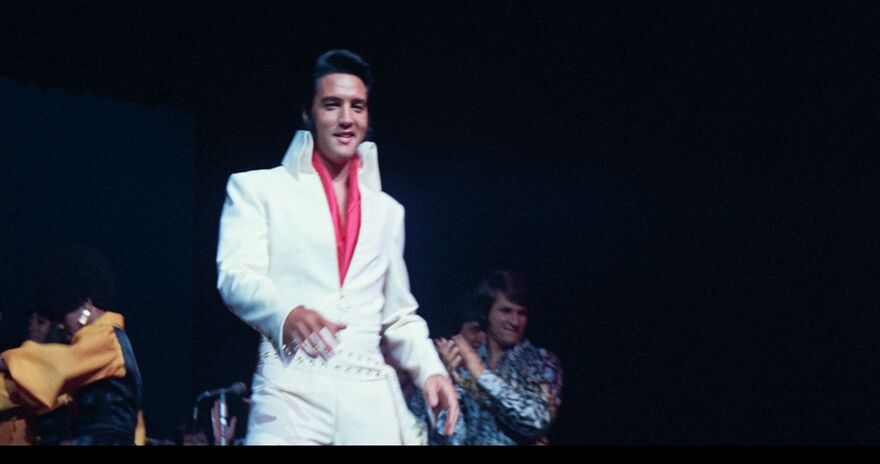 Elvis Presley in his iconic white jumpsuit performs on stage. 