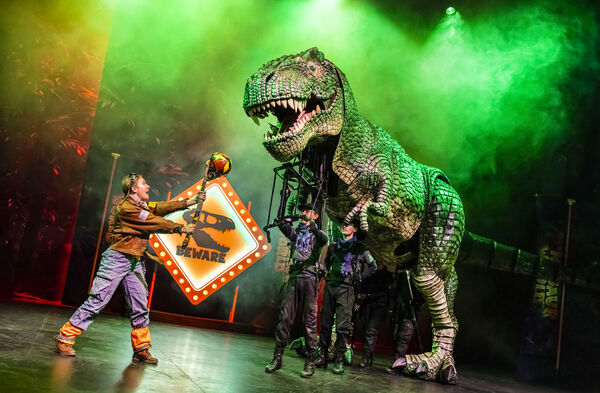 Large T-Rex puppet with woman holding a balloon on a stick up to it