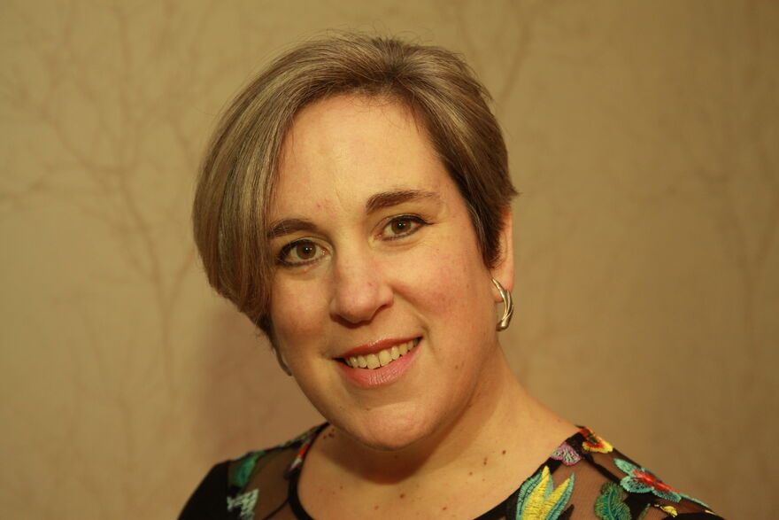 Image of a white woman with short hair and a side parting smiling at the camera