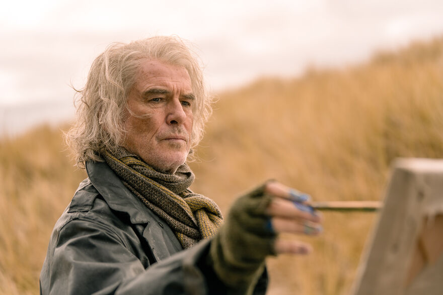 An older man paints in a grassy field.
