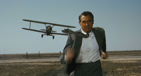 A man in a suit runs away from a low flying propeller plane on an air field. A man in a suit runs away from a low flying propeller plane on an air field.