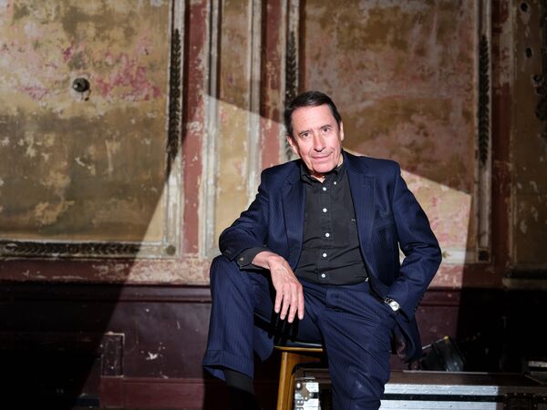 Jools Holland in a navy blue suit sat on a table