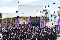 Graduands standing in a group throwing their caps in the air in front of Warwick Arts Centre