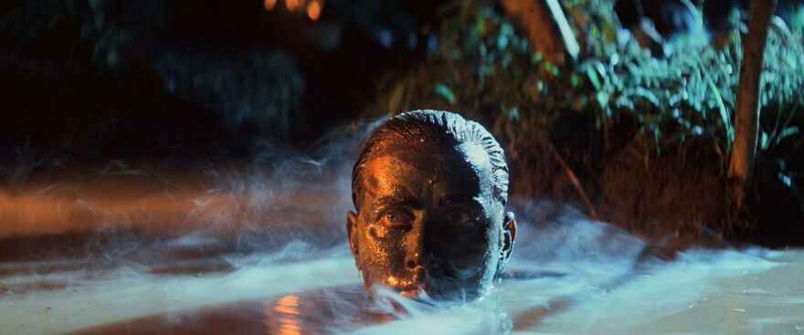 A man with his head above water. His face is covered in mud.