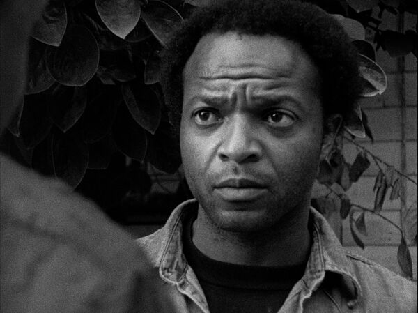 A close up of a man with furrowed brow. He is looking at a figure with back to camera.  