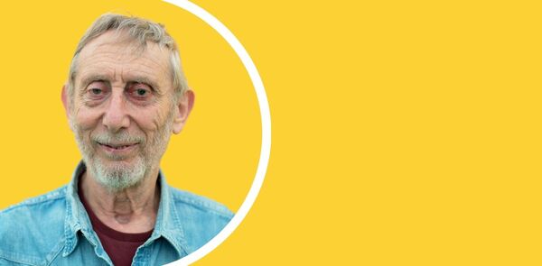Michael Rosen in a light blue denim shirt with a yellow background and white semi circle