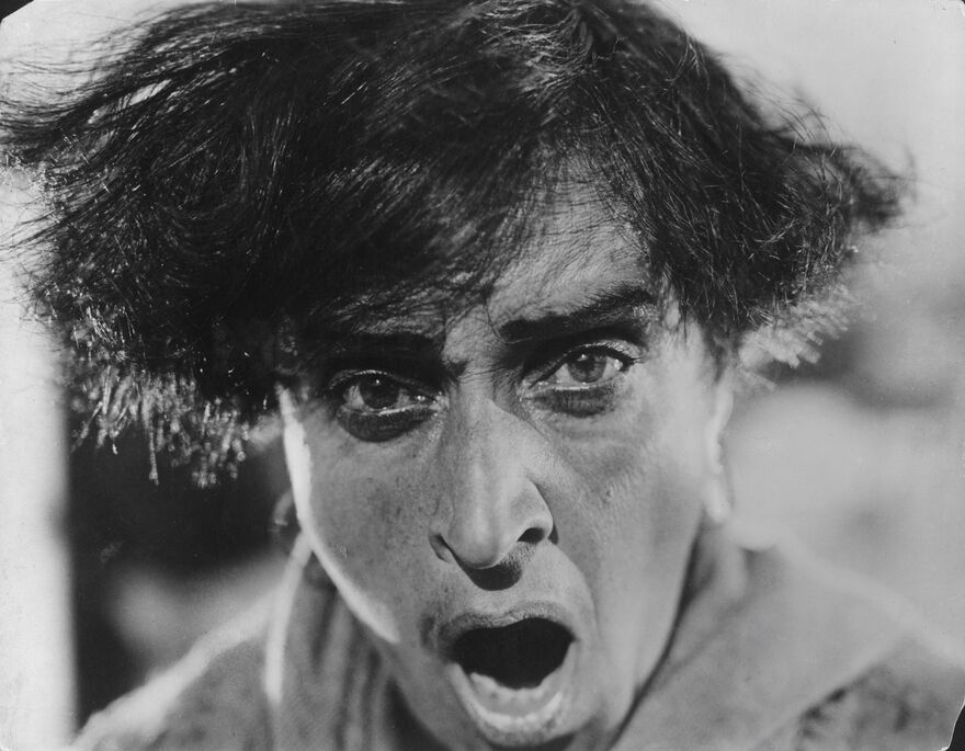 A black and white image of a man with his mouth open and eyes wide.
