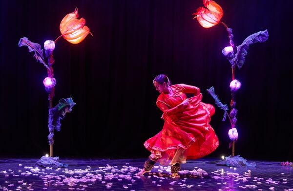 A woman dancing in a flowing red dress in between two large flower lights