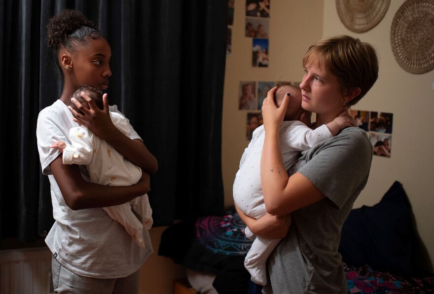 Two young women look to each other as they cradle their babies.