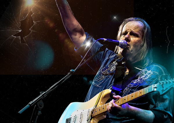Walter Trout with guitar singing into a microphone, on the left-hand side is broken glass 