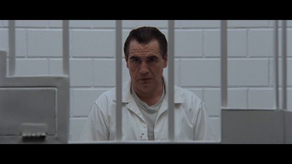 A man dressed in all white sits in a locked cell. 