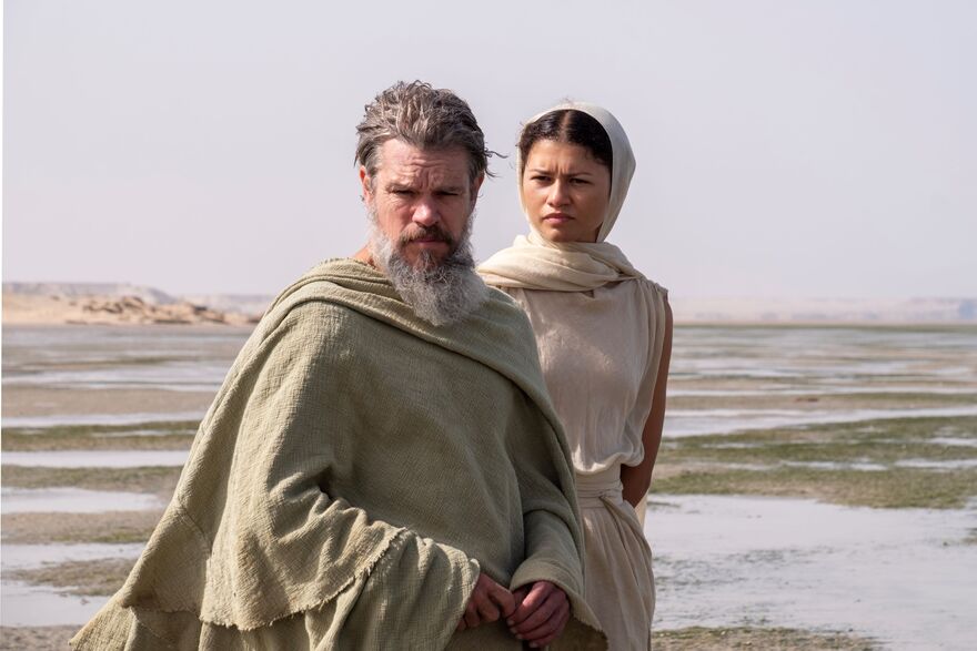 Matt Damon as Odysseus and Zendaya as Athena stand on a beach. 
